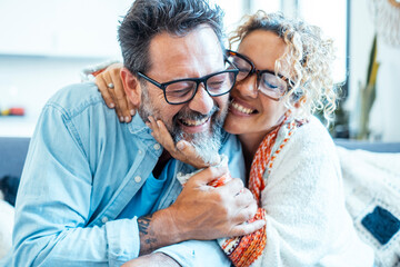 A smiling, happy couple sharing a warm and comfortable moment on their sofa at home, demonstrating...