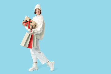 Beautiful young happy woman with shopping bags and gift box on blue background. Christmas celebration