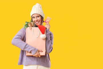 Beautiful young happy woman with shopping bag of decorations and credit card on yellow background. Christmas celebration
