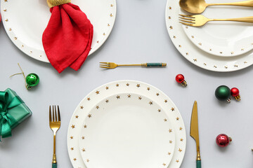 Beautiful table setting with Christmas balls and gift box on grey background