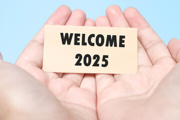 Hand holding a note Welcome 2025 with a blue background. New year concept with typographic 2025. Motivational words to welcome the new year 2025