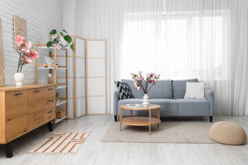 Interior of living room with sofa, commode and magnolia flowers in vases