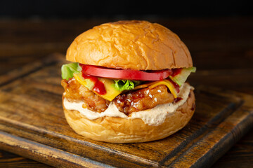 Burger, hamburger with breaded chicken, tomato, cheese, lettuce on a wooden board on a wooden table.