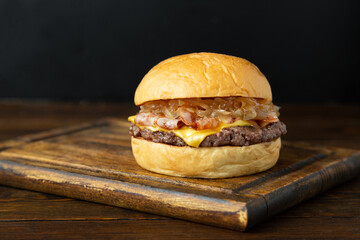 Burger, hamburger with meat patty, cheese, bacon and fried onions on a wooden board on a wooden table.