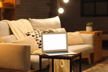 Laptop with blank screen on coffee table in modern living room at evening
