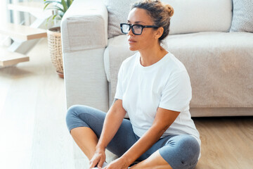 In her apartment, the woman practices her daily physical routine, sitting on the floor in sportswear, engaging in yoga or pilates to enhance both physical fitness and mental wellness