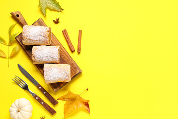 Wooden board with cut tasty pumpkin strudel, cinnamon and autumn leaves on yellow background