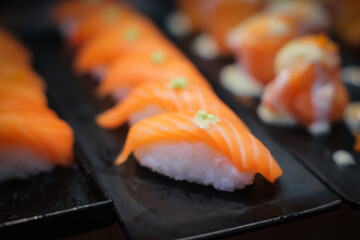 Salmon sushi topped with sauce and mayonnaise is arranged on a tray, ready for customers to serve...