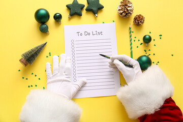 Santa Claus writing to-do list with Christmas decor on yellow background