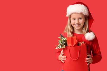 Cute girl in Santa hat with shopping bag on red background. Christmas celebration