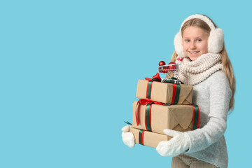 Cute girl holding gift boxes and mini shopping cart with Christmas balls on blue background