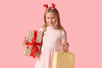 Cute girl in reindeer horns with shopping bag and gift box on pink background. Christmas celebration