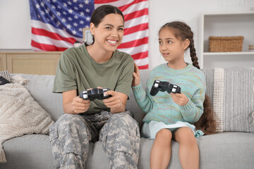 Female soldier with her daughter playing video game on sofa at home