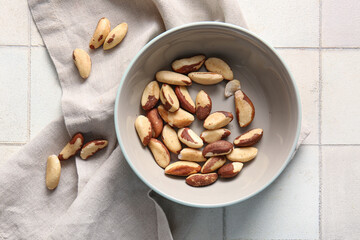 Bowl with tasty Brazil nuts on white tile background