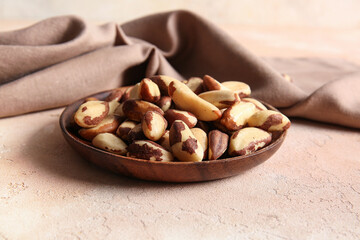 Wooden plate with tasty Brazil nuts on beige background
