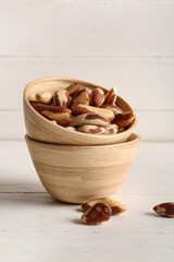 Bowl with tasty Brazil nuts on white wooden background