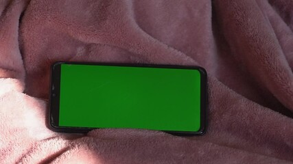 A smartphone with a green screen lies on the bed. Top view