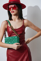 Woman in red dress, red hat, and red sunglasses holding green handbag, wearing red leather outfit