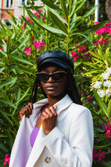 Stylish businesswoman exuding confidence in urban chic attire, standing near blooming oleander