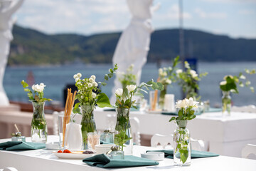 A minimalist outdoor wedding table with white linens, green accents, and floral arrangements, set...