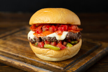 Burger, hamburger with meat patty, tomatoes in salsa sauce, pickled cucumber on a wooden board on a wooden table.