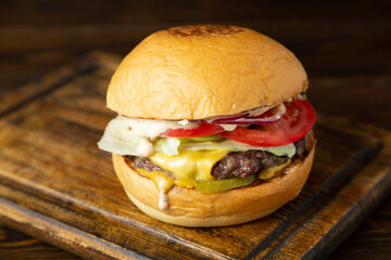 Burger, hamburger with meat cutlet, tomatoes, pickled cucumber, sour cream and onion on a wooden board on a wooden table.