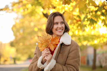 Beautiful young happy woman with fall leaves in autumn park