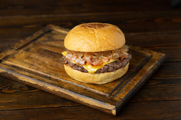 Burger, hamburger with meat patty, cheese, bacon and fried onions on a wooden board on a wooden table.