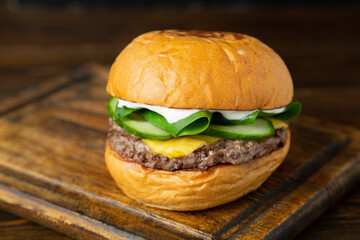 Burger, hamburger with meat patty, cheese, cucumber and spinach leaves on a wooden board on a wooden table.