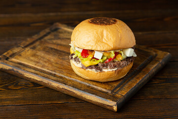 Burger, hamburger with meat patty, cheese, feta cheese, corn and lettuce on wooden board on wooden table.