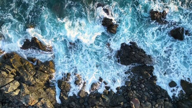 Aerial view of crashing waves against rocky shoreline at sunset with vibrant colors and natural beauty captured along the coast
