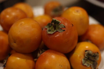 A stunning, vibrant display of ripe, succulent persimmons in bright goldenorange, accompanied by fresh green leaves