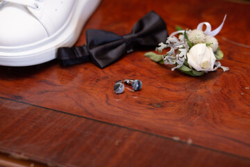 Elegant Groom Accessories: Black Bow Tie, Floral Boutonniere, and Cufflinks on Wooden Surface -...