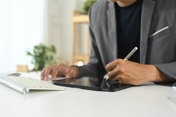 Cropped shot businessman in suit working on digital tablet with stylus pen in bright workspace