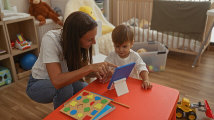 Woman engaging with her son using a digital tablet in a cozy bedroom filled with toys, fostering learning and connection in a lively, indoor family environment.