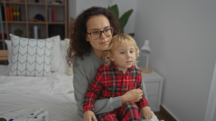 Mother and son sitting together on bed in cozy bedroom, showcasing love and family bond indoors with a warm atmosphere.