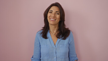 Woman smiling against a pink wall, middle aged, wearing a blue blouse, isolated, mature, hispanic,...