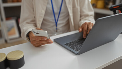 Hispanic man using laptop and phone in home decor setting, hands visible on both devices in modern interior