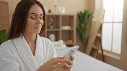 Woman in a spa wearing a robe and using a smartphone in an indoor beauty center with a peaceful wellness ambiance.