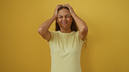 Frustrated young woman stands over isolated yellow background with hands on her head