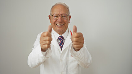 Smiling elderly caucasian man in a white lab coat and glasses giving thumbs up in front of a plain...
