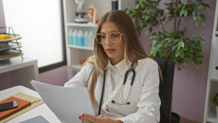 Woman doctor reviewing documents in a hospital room wearing glasses with a stethoscope, highlighting a professional and clinical environment featuring a hispanic female healthcare worker.