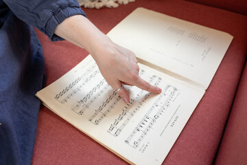 A close-up of a hand pointing to a specific line in a sheet music book, focusing on musical notes....