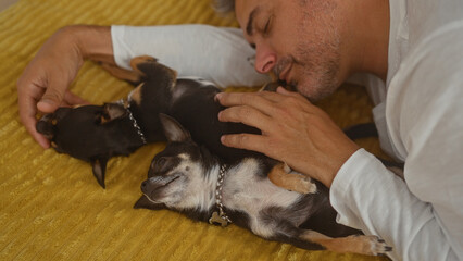 Middle-aged hispanic man relaxing in bed with two chihuahuas at home, showing a tender moment with his pets in an indoor bedroom setting.