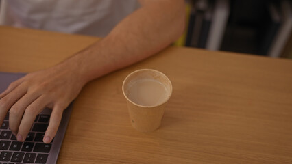 A young hispanic man working on a laptop at an office desk with a cup of coffee in an indoor workplace setting.