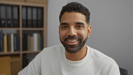 Young hispanic man smiling in modern workplace with bookshelf in background