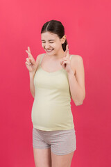 Cheerful young pregnant woman holding fingers crossed, waiting pregnancy isolated on colored background in studio. lifestyle pregnancy concept