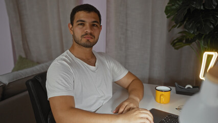 Handsome hispanic man sitting in a cozy living room at home with a laptop and coffee mug on the table