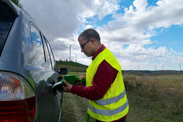 Technician refueling car near wind turbines symbolizing green energy transition