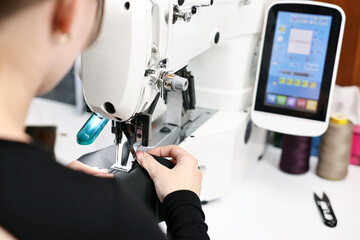 Woman working with sewing machine at white table in professional workshop, closeup